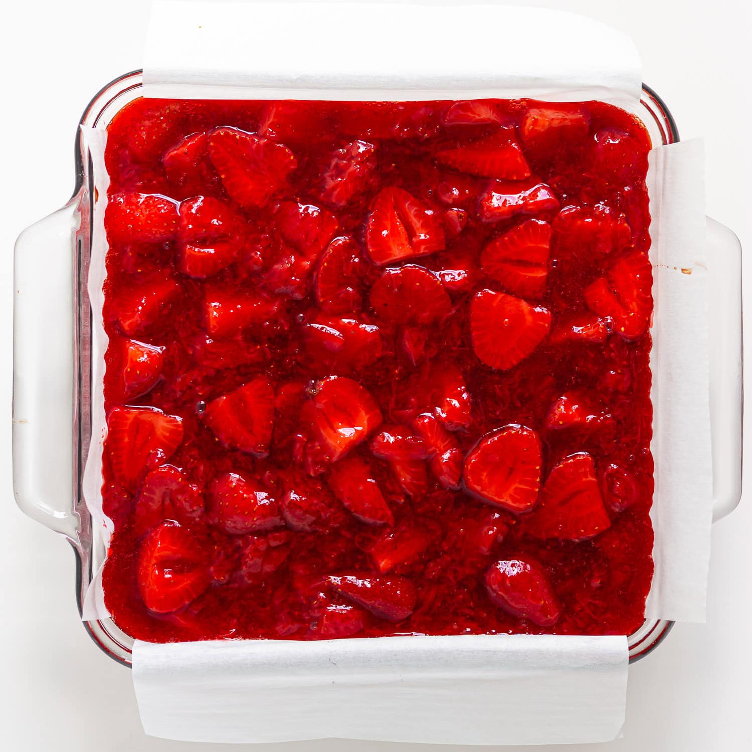 Strawberry cheesecake bars in square glass baking dish before being sliced.