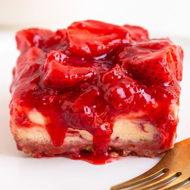 Closeup of a strawberry cheesecake bar with a gold colored fork in the corner.