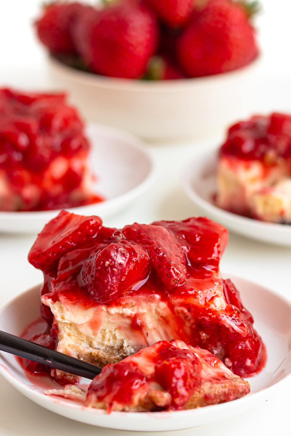 Strawberry cheesecake bars on serving plates with scoop on fork.