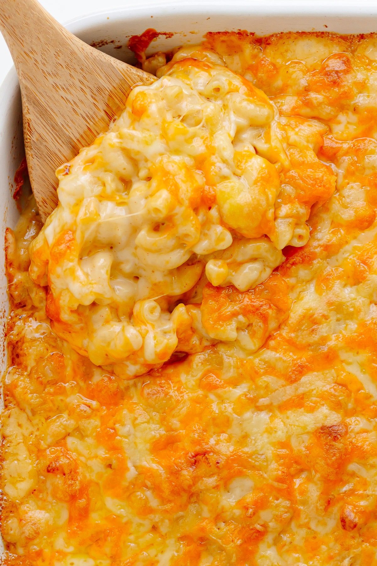 3 cheese mac and cheese in a white casserole dish with wooden spoon lifting some out of the corner.