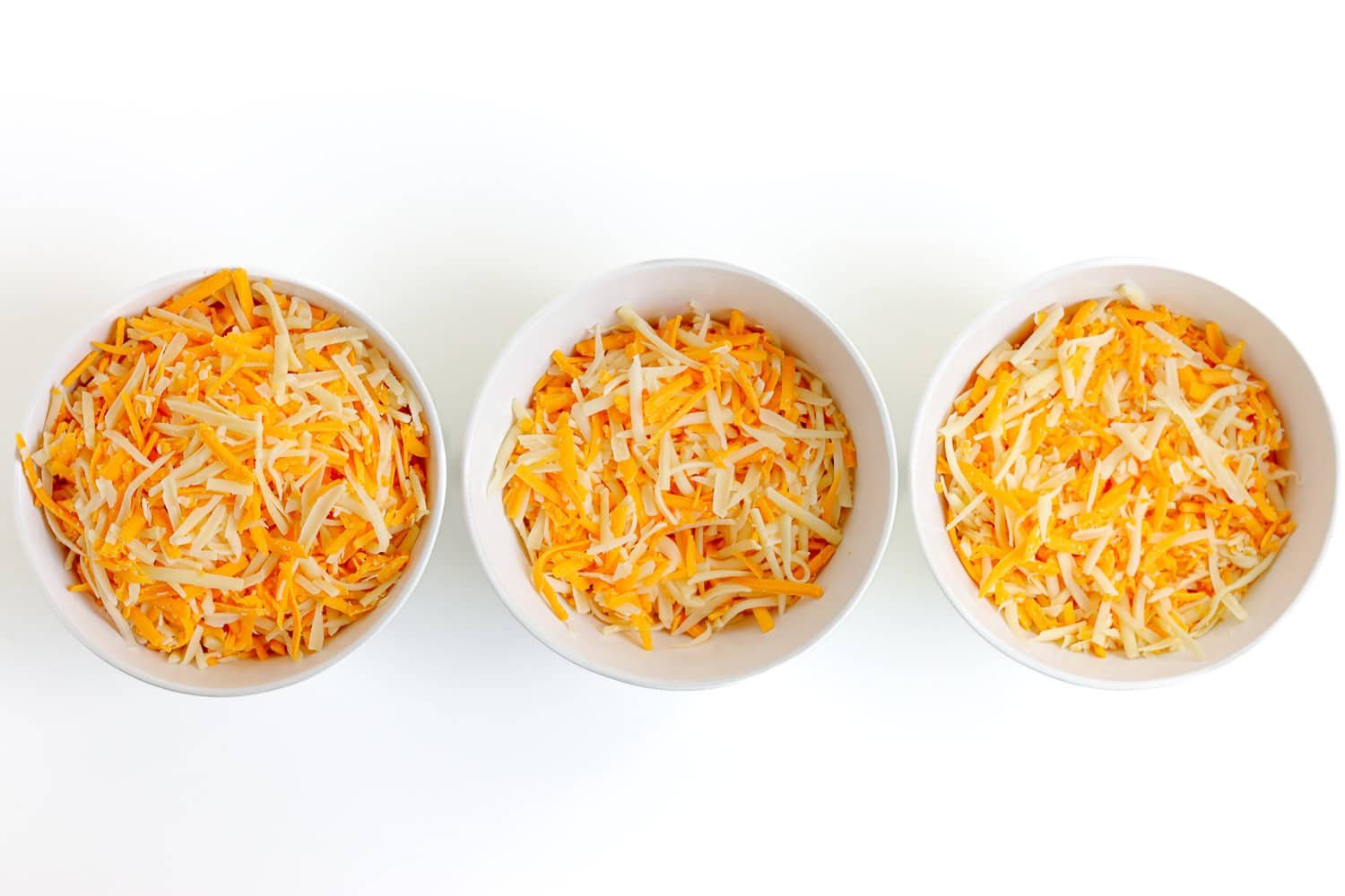 Three cheeses combined and portioned into three white bowls for baked mac and cheese.