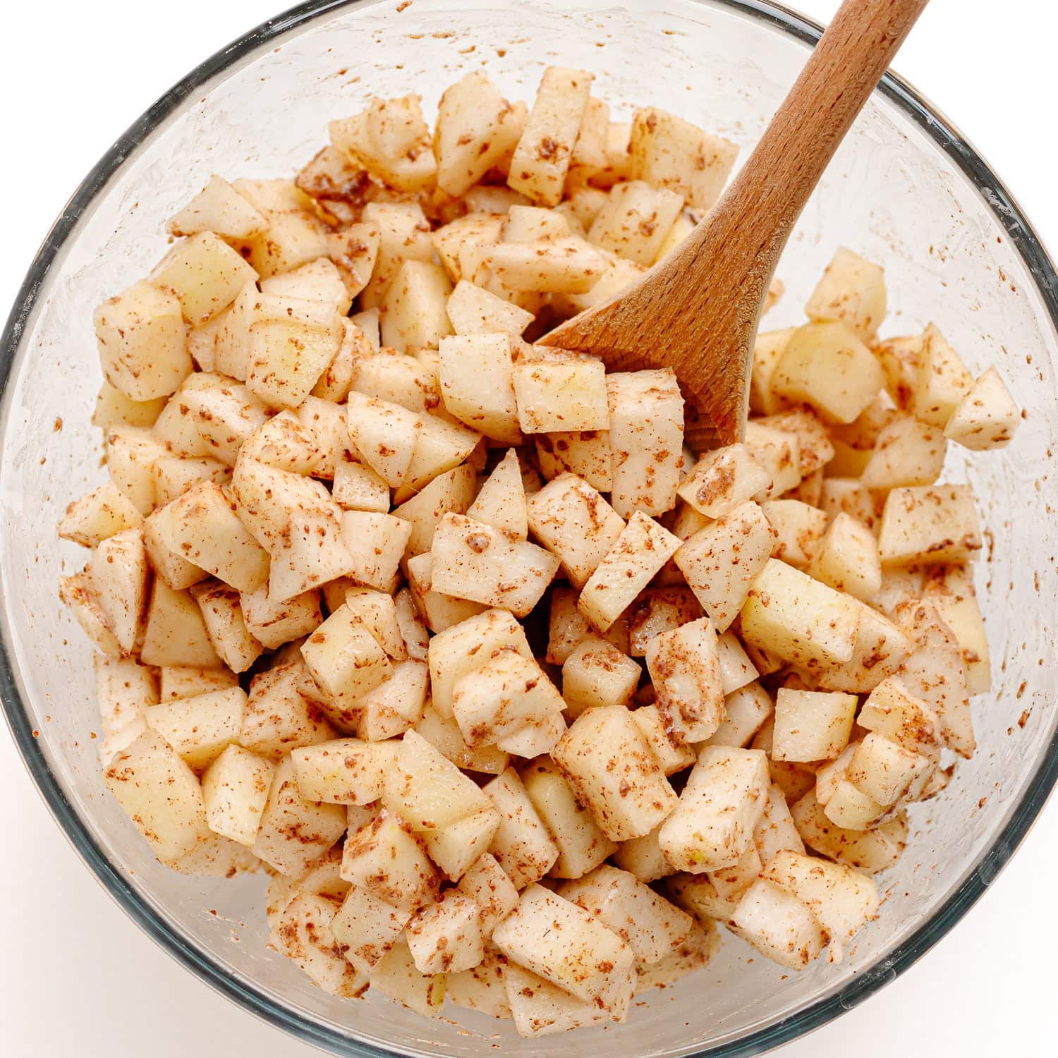 Pear mixture for pear crumble in glass mixing bowl with wooden spoon.