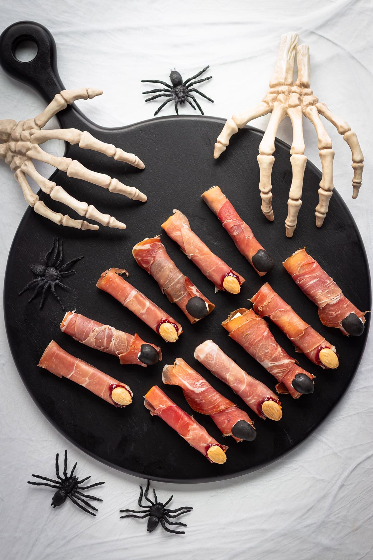 Prosciutto and cheese Halloween fingers arranged on a black serving board on a spooky decorated surface.