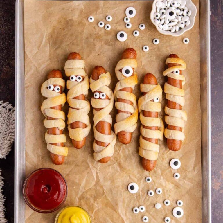 Hot dog mummies on a parchment paper lined baking sheet.