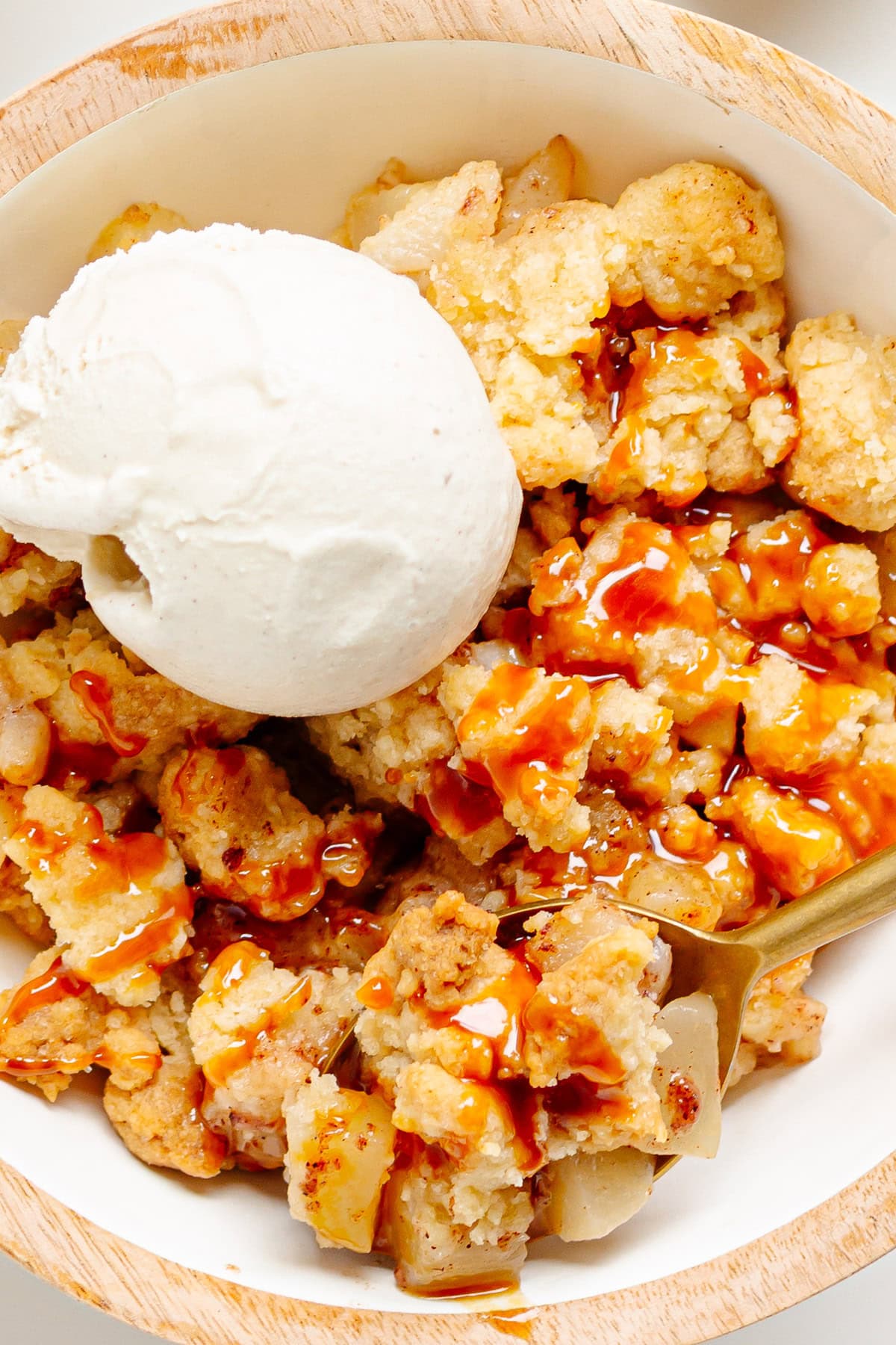 Bowl of pear crumble topped with vanilla ice cream and a drizzle of caramel sauce.