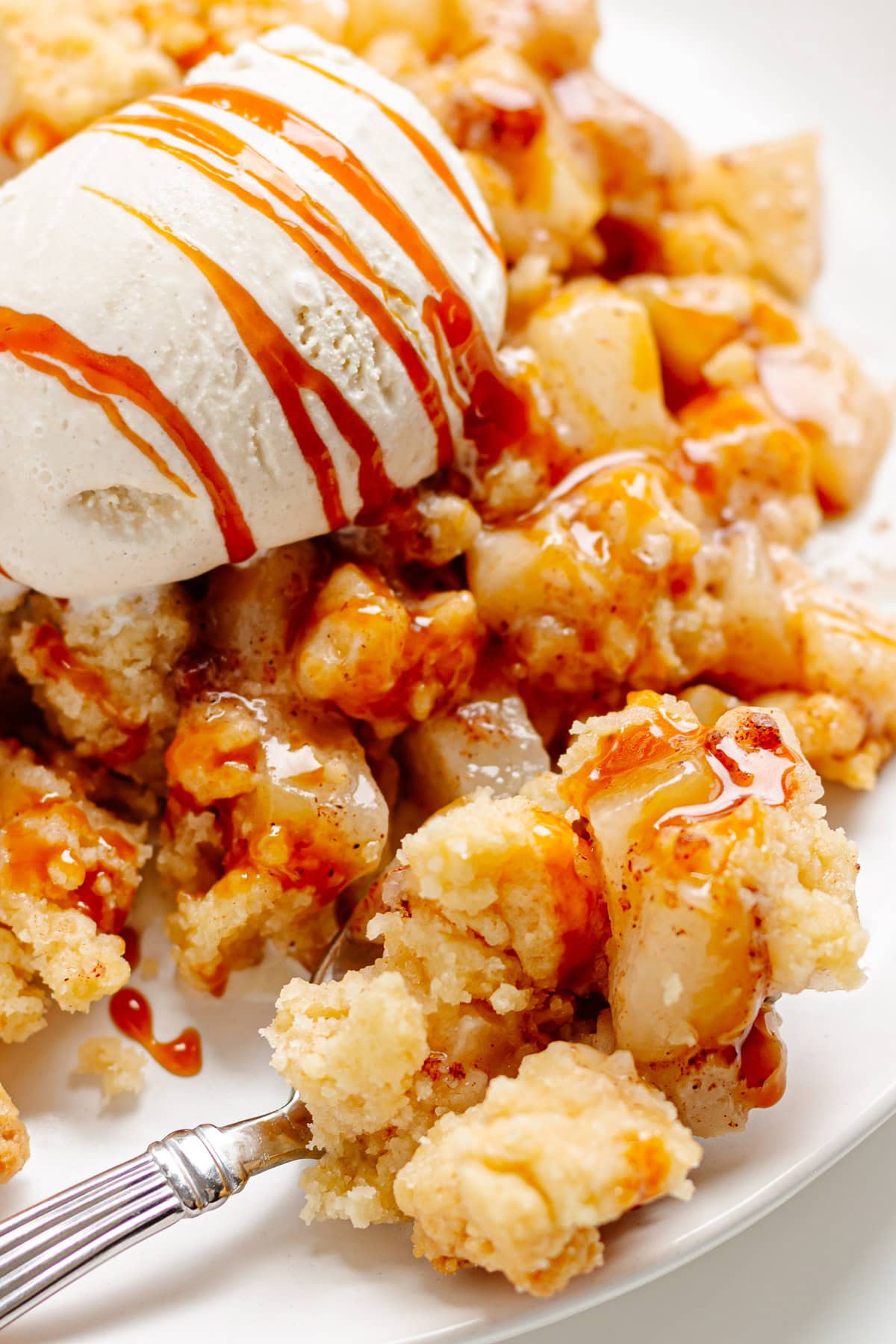 Pear crumble with butter streusel on a white dessert plate topped with vanilla ice cream and salted caramel sauce.