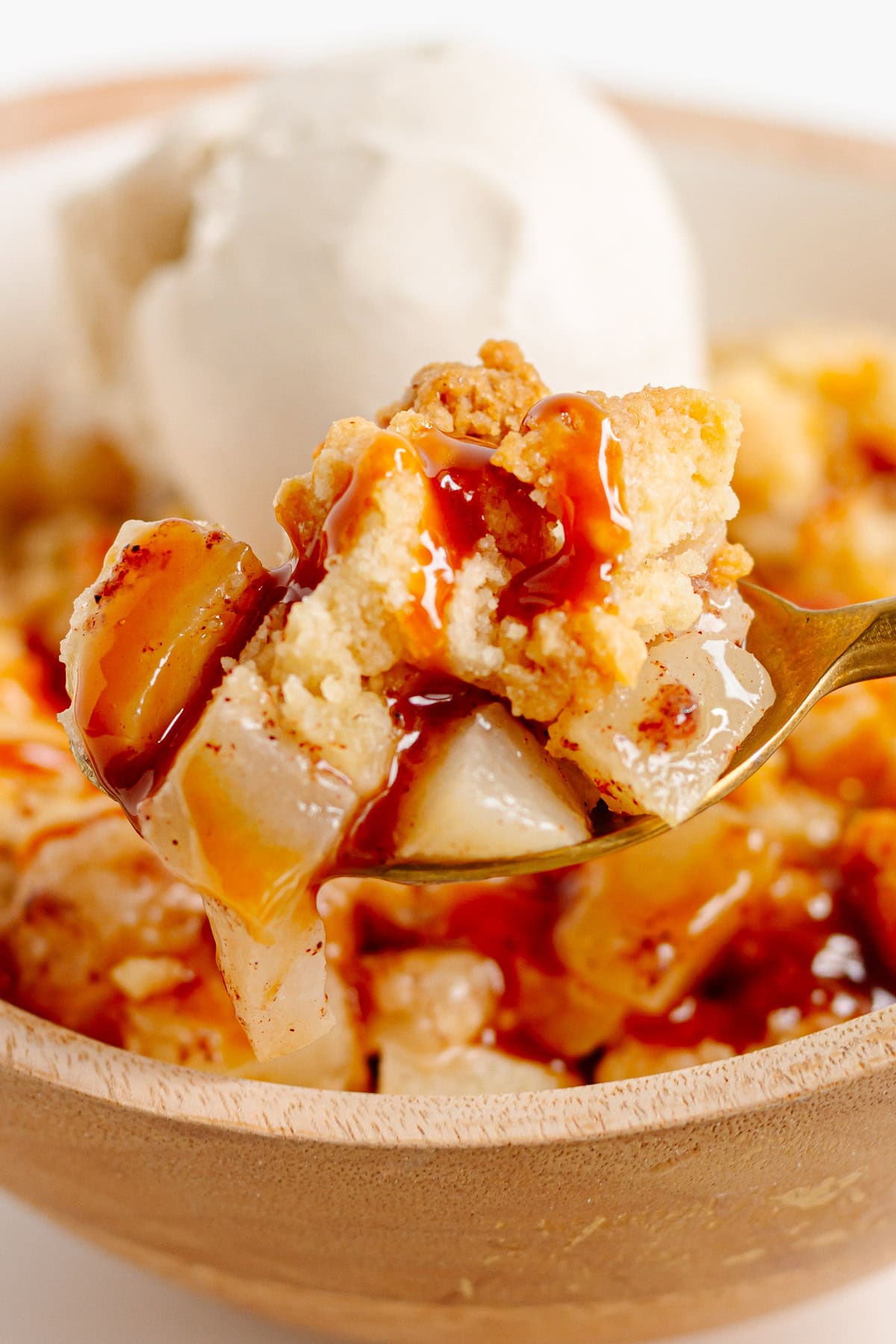 Pear crumble with ice cream and caramel sauce being scooped up with a spoon from a bowl.