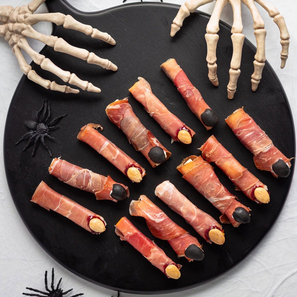 Savory Halloween witch fingers on a black serving board with skeleton hands reaching in.