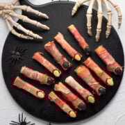 Savory Halloween witch fingers on a black serving board with skeleton hands reaching in.