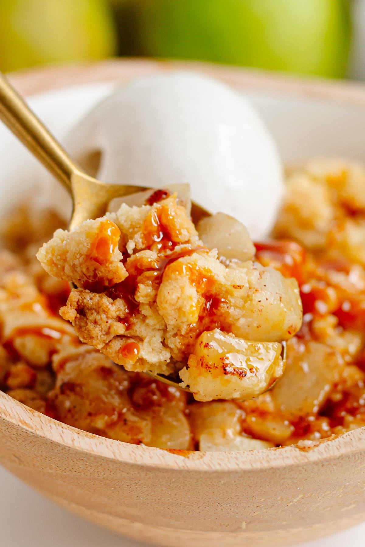 Spiced pear crumble with a scoop of vanilla ice cream in a wooden dessert bowl.