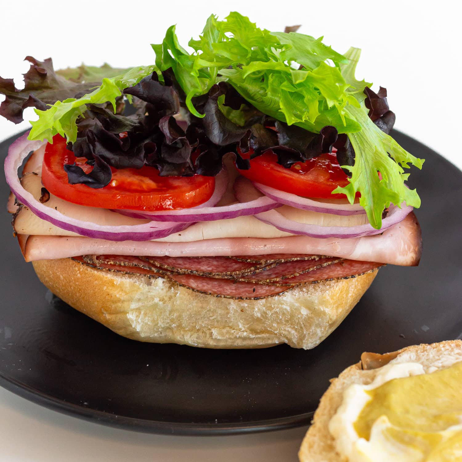 Sandwich being built on a kaiser bun with top off to the side.