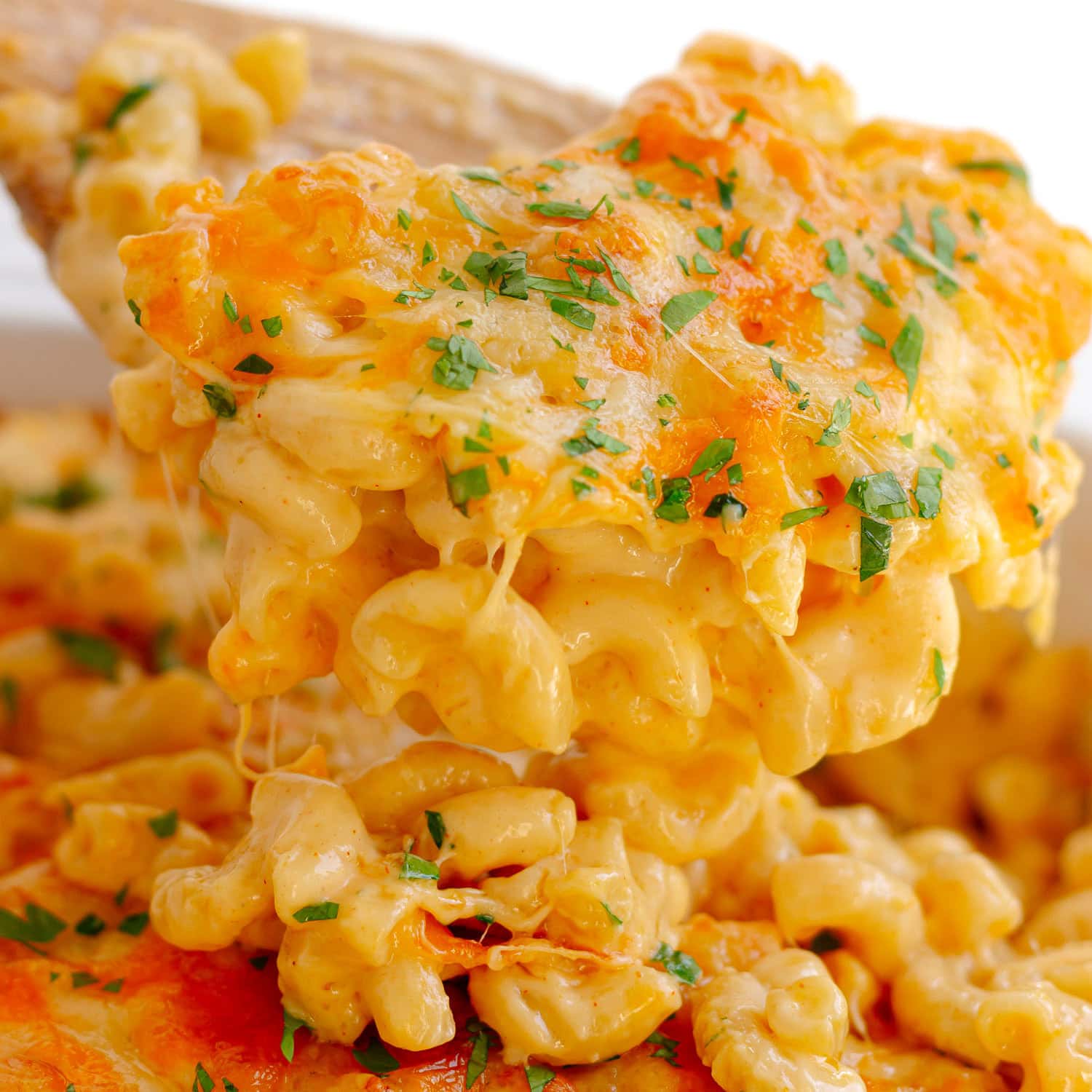 Scoop of three cheese baked mac and cheese being lifted from baking dish.