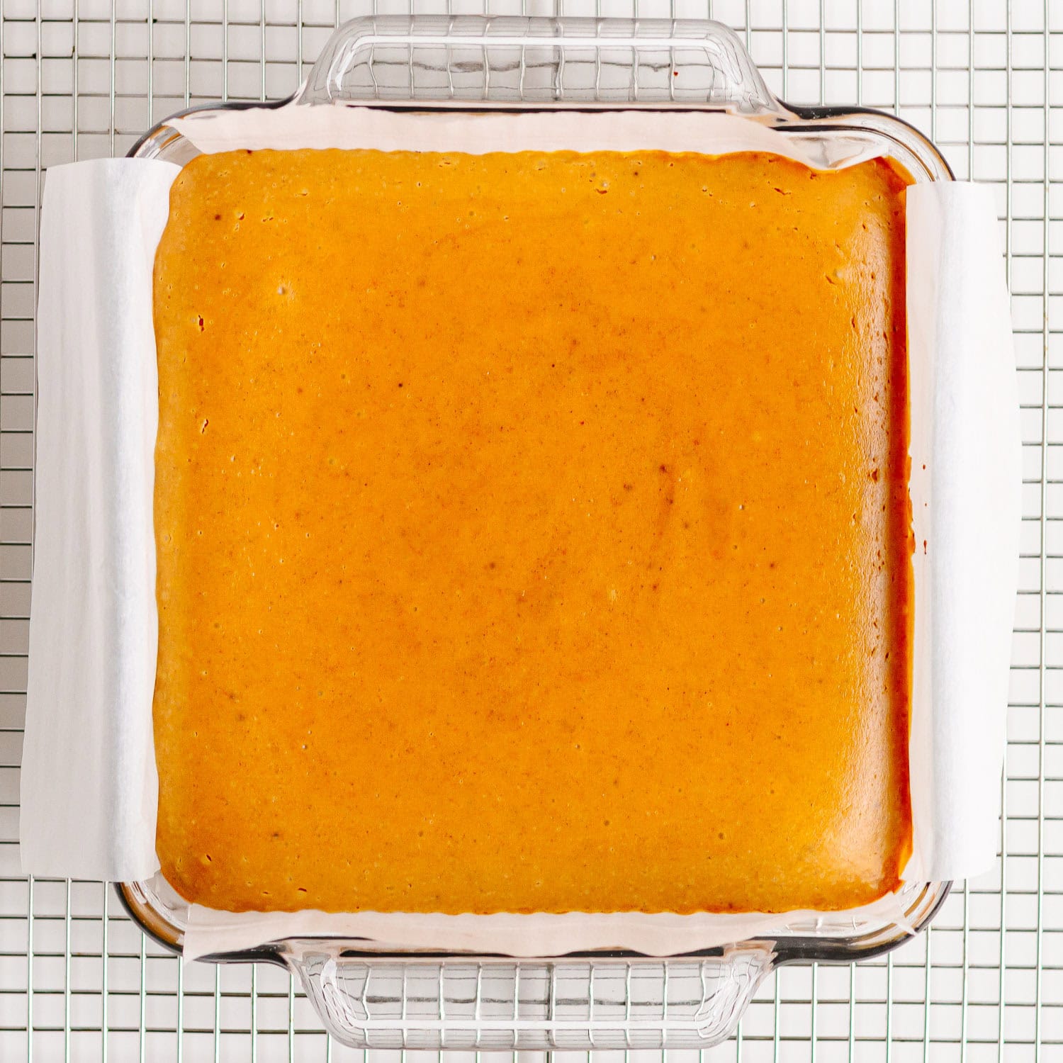Glass baking dish of baked pumpkin cheesecake bars cooling on a wire rack.
