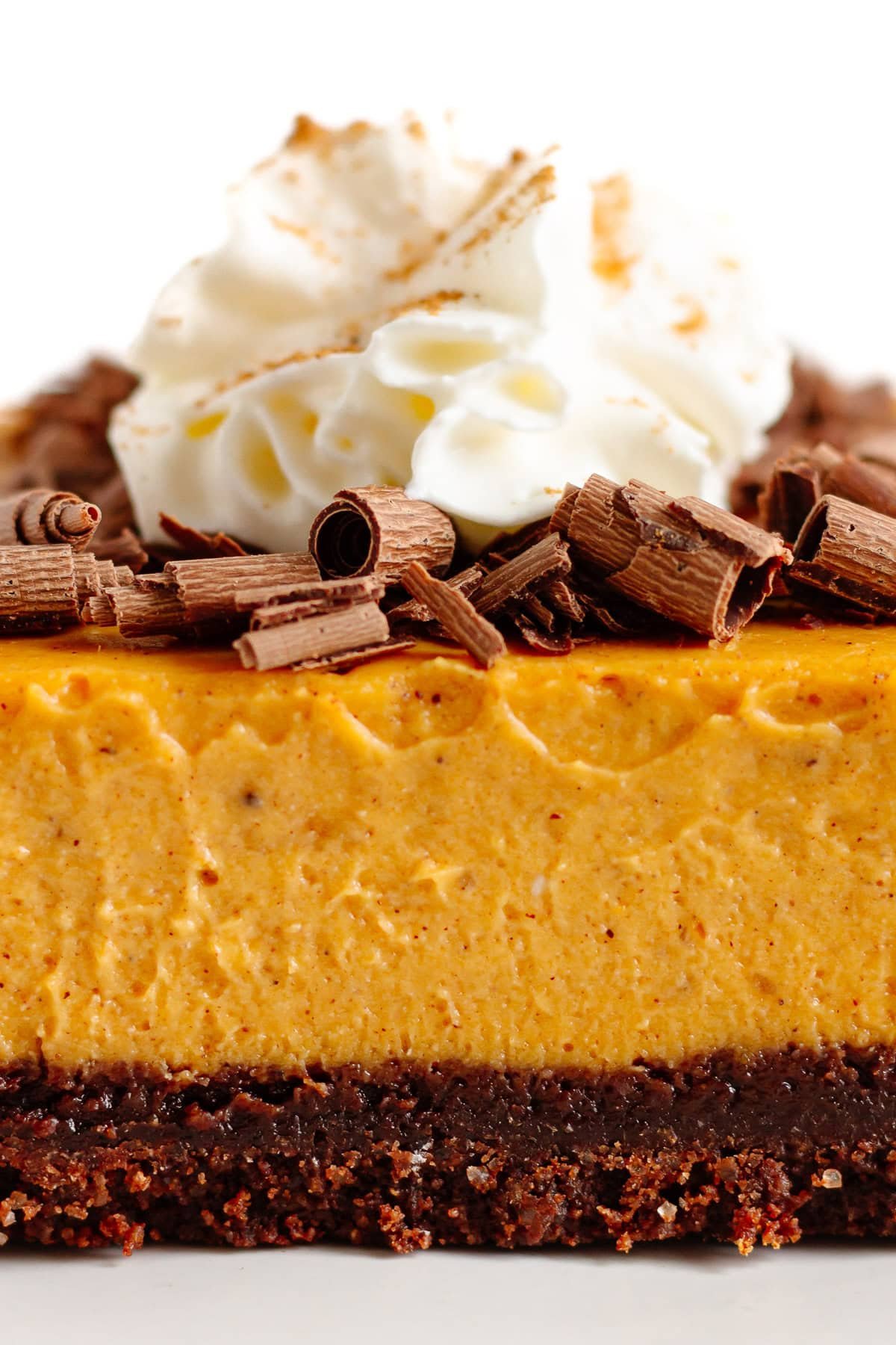 Closeup of a pumpkin cheesecake bar with chocolate graham cracker crust and garnish of chocolate shavings and whipped cream on top.