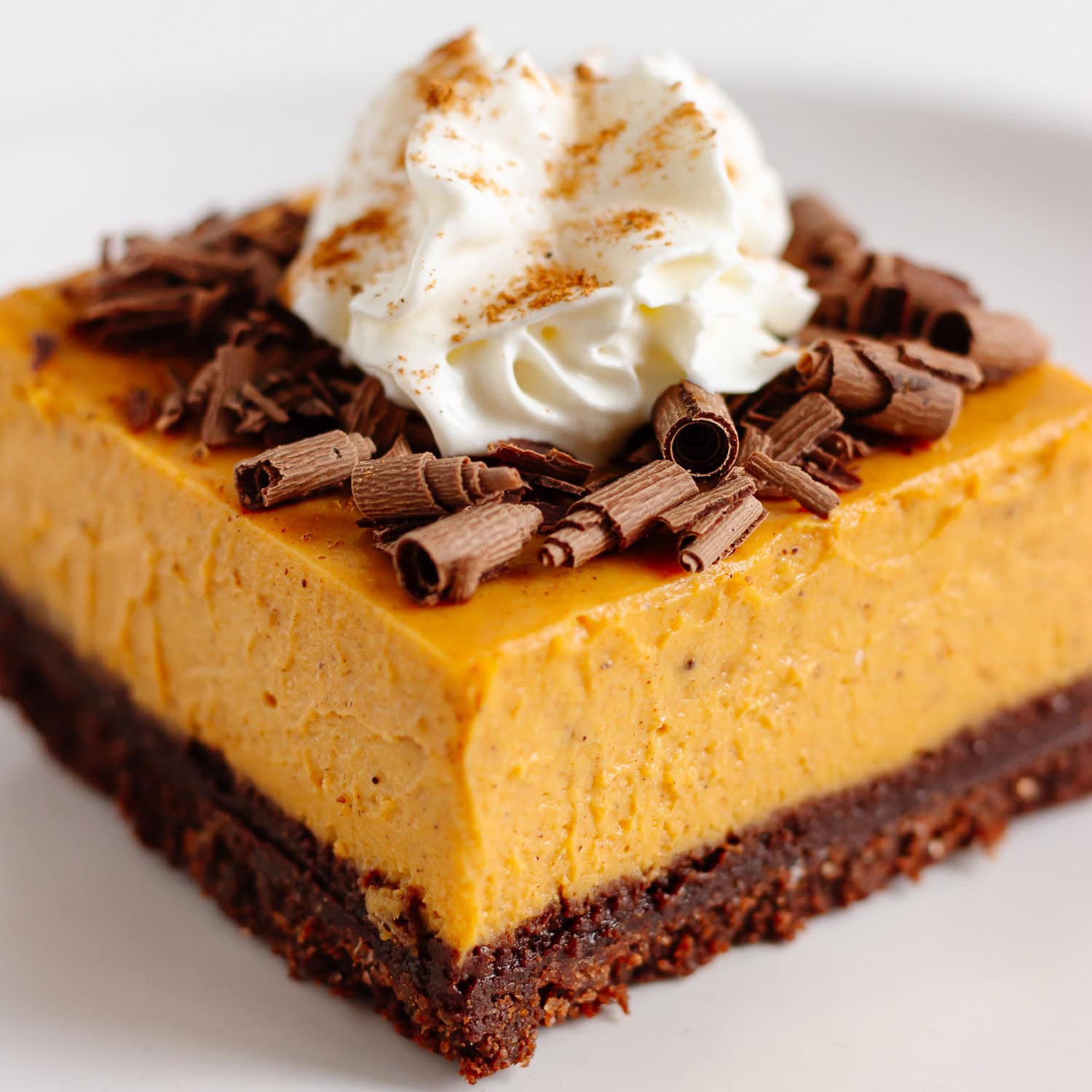 Closeup of a chocolate pumpkin cheesecake bar on a white plate.
