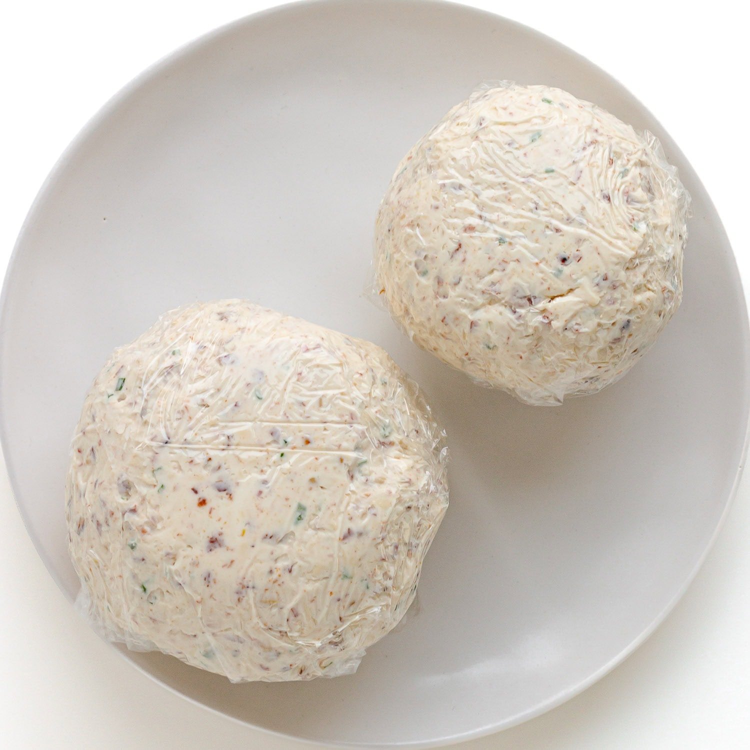 Two cheese balls wrapped in plastic wrap on a plate.