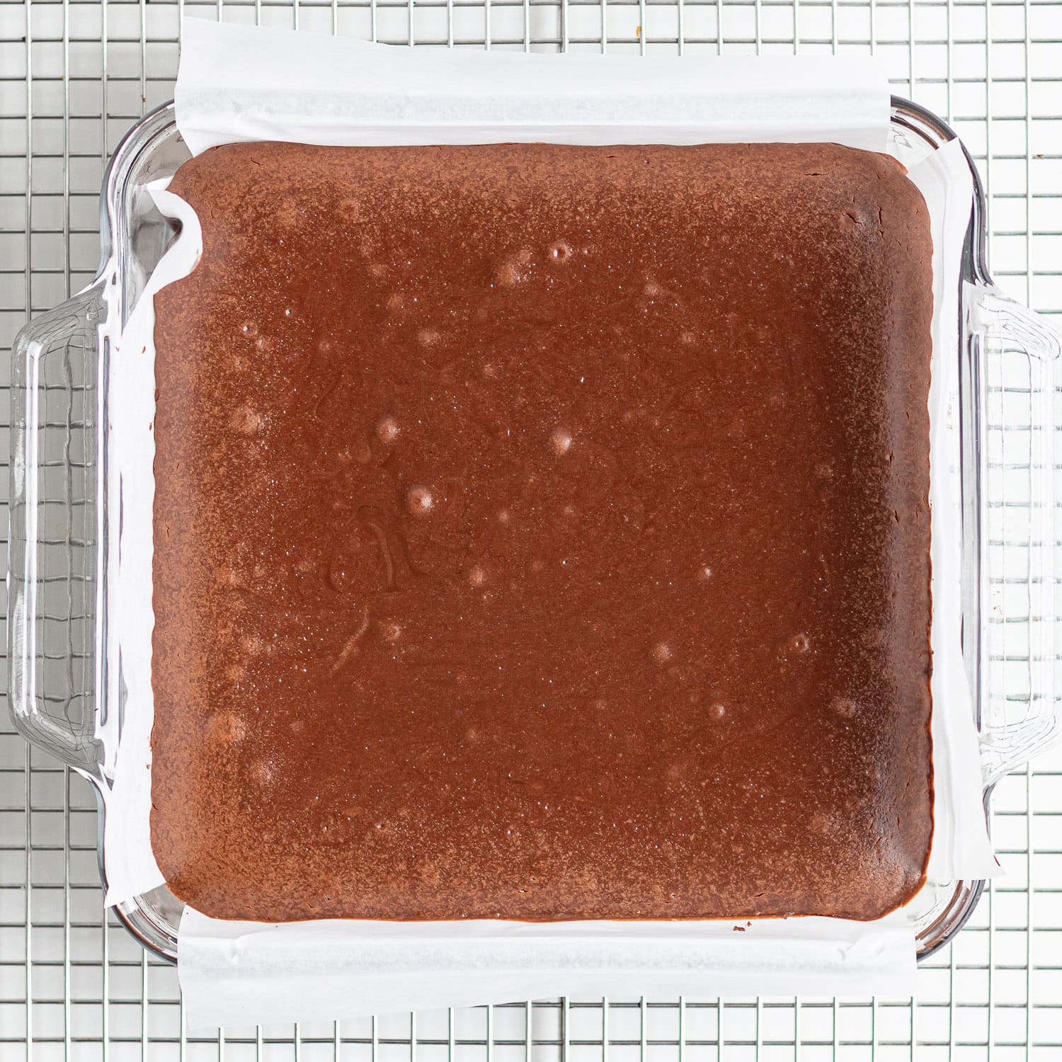 Square baking dish of chocolate cheesecake cooling on a rack.