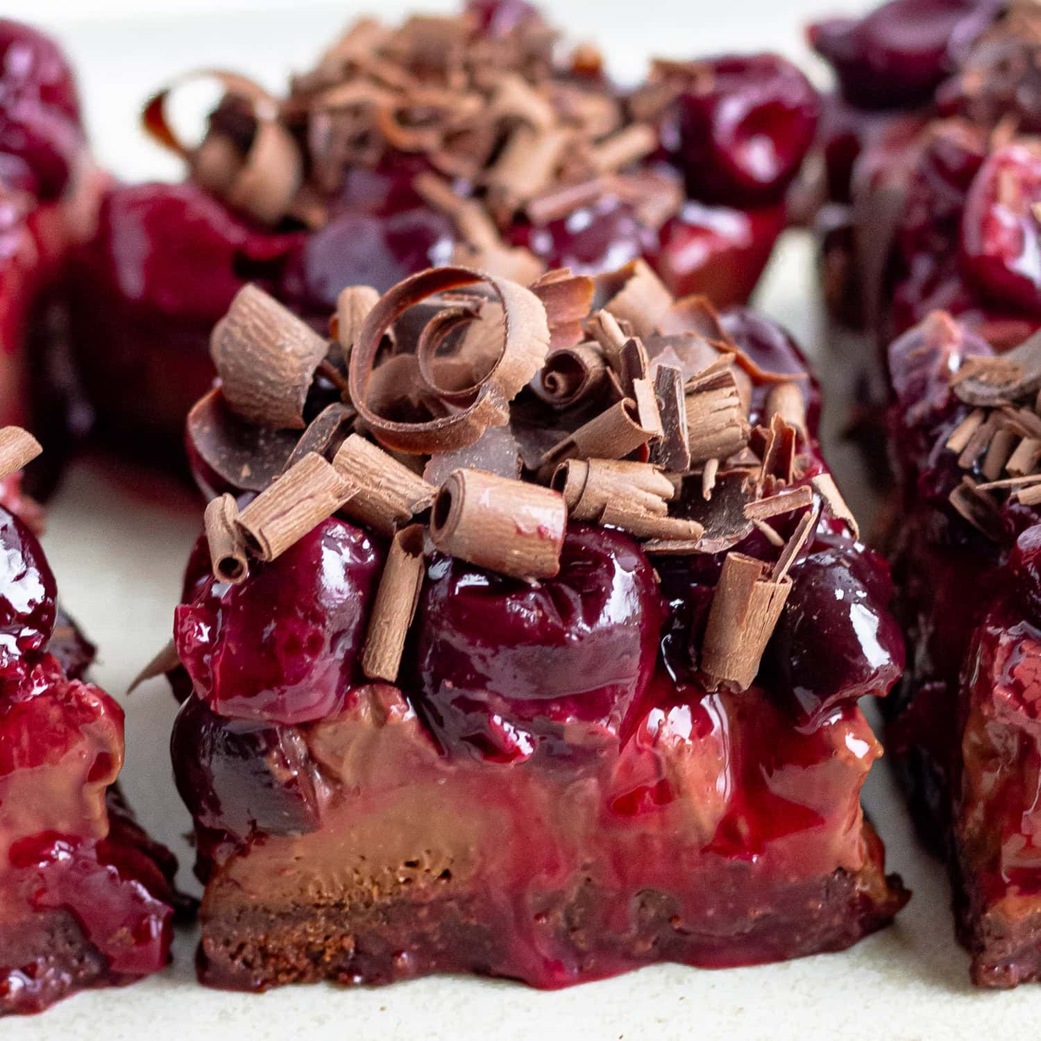 Chocolate cherry cheesecake bars garnished with chocolate shavings on a platter.