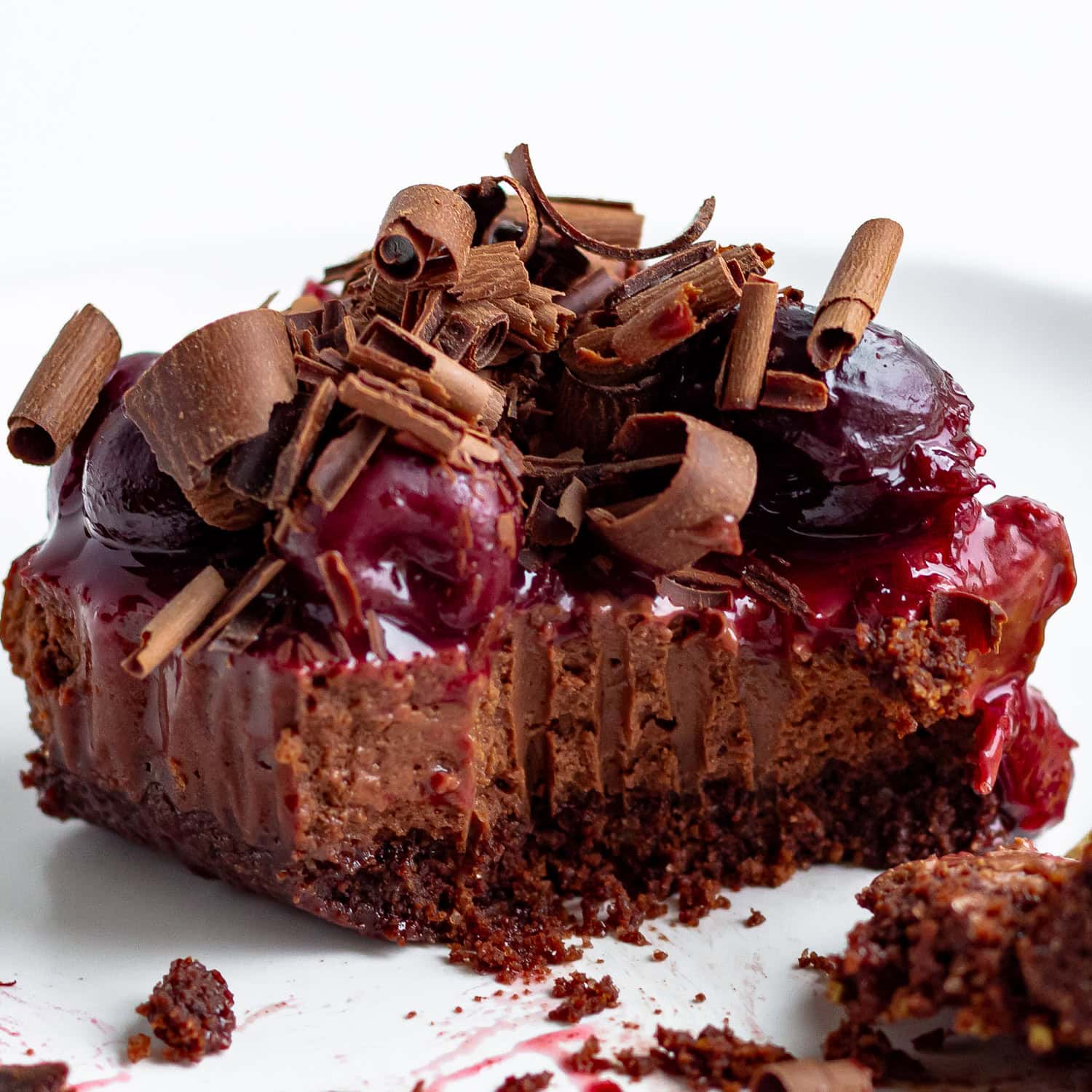 Square slice of chocolate cherry cheesecake on a white plate with fork removing a bite.