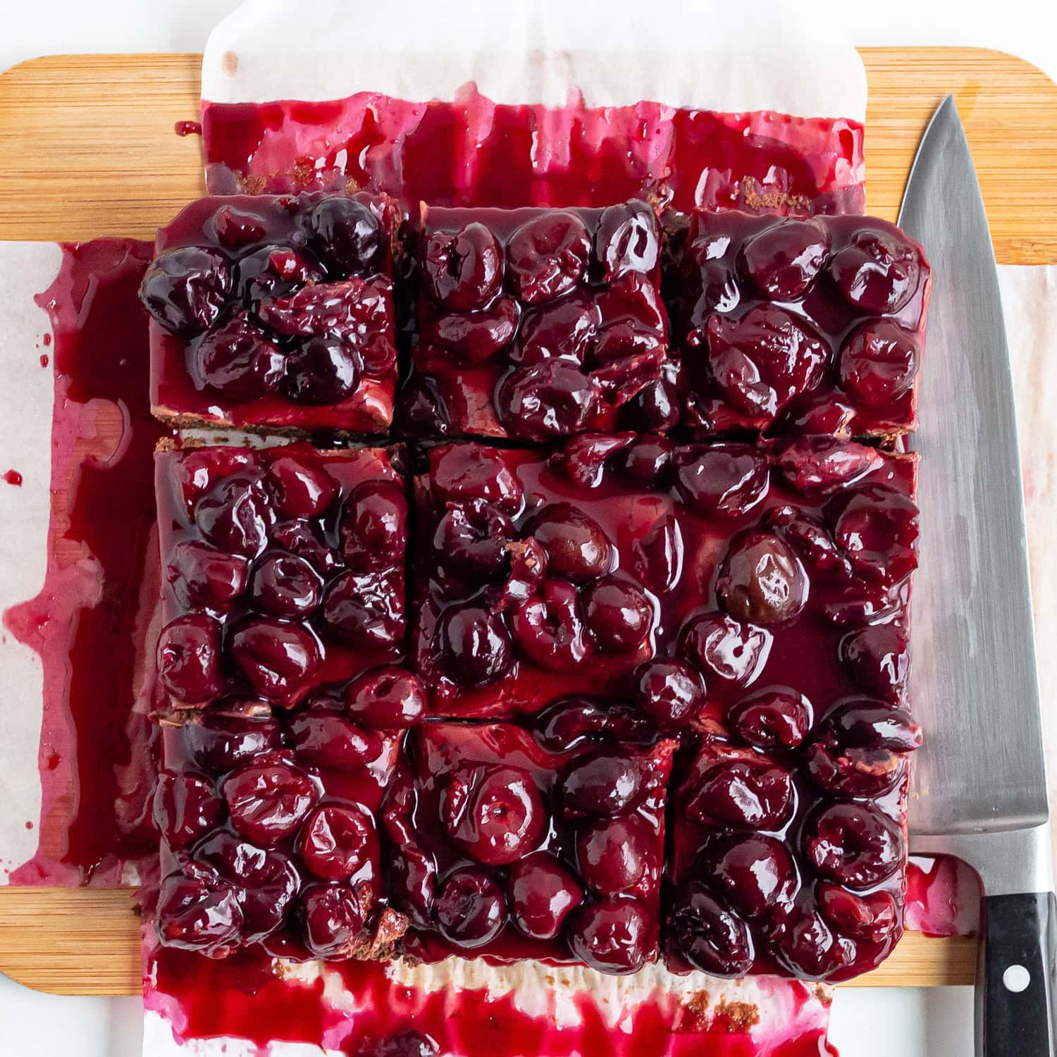 Chocolate cherry cheesecake on a cutting board sliced into squares.