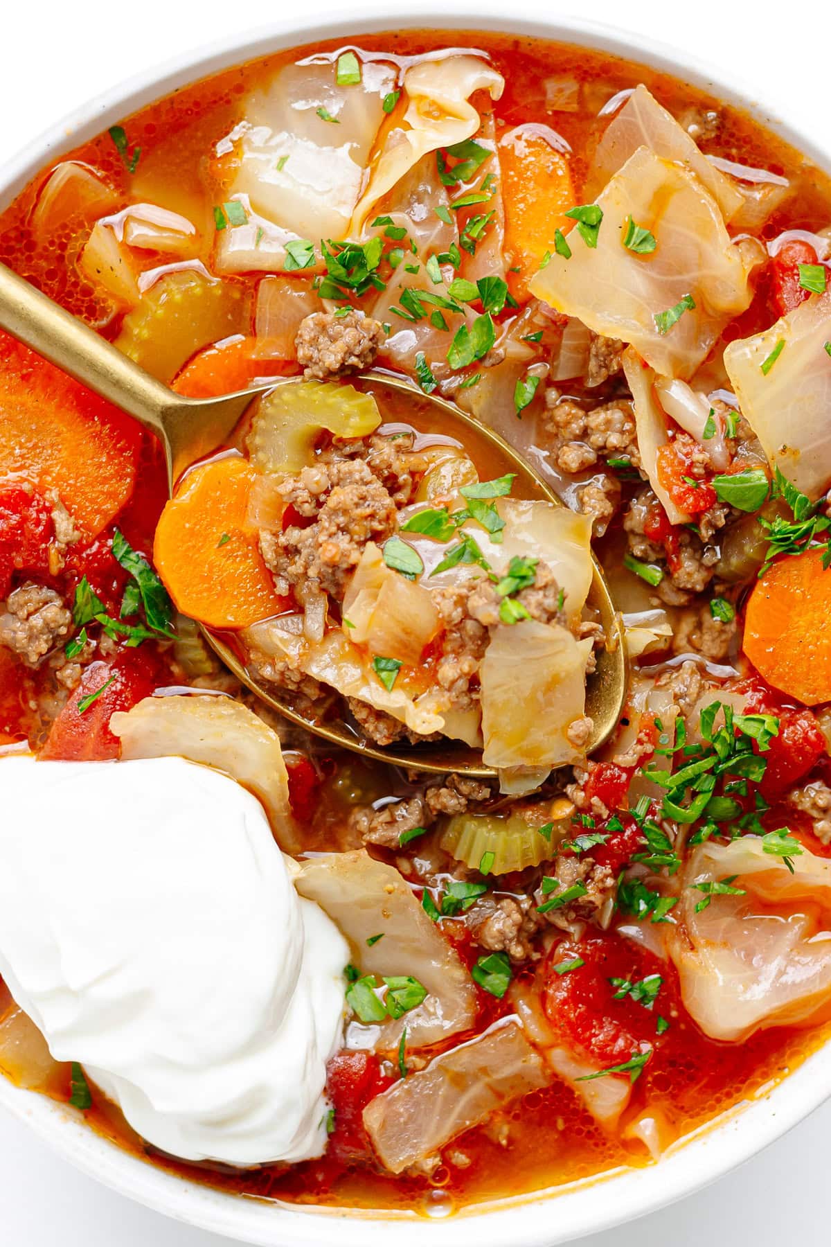 Bowl of beef cabbage soup garnished with chopped parsley and a dollop of sour cream.