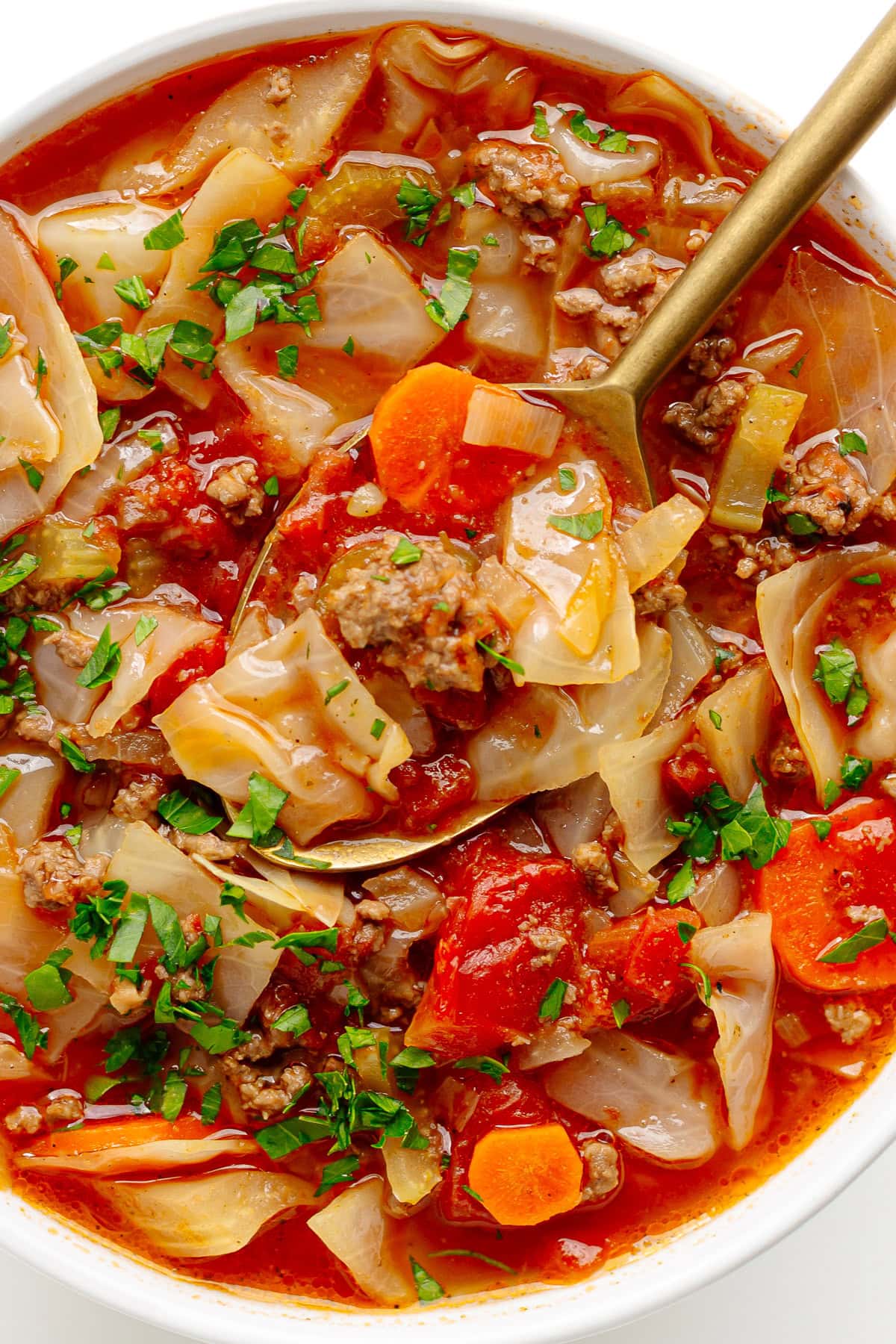 Cabbage and ground beef soup in a white bowl with a spoon.