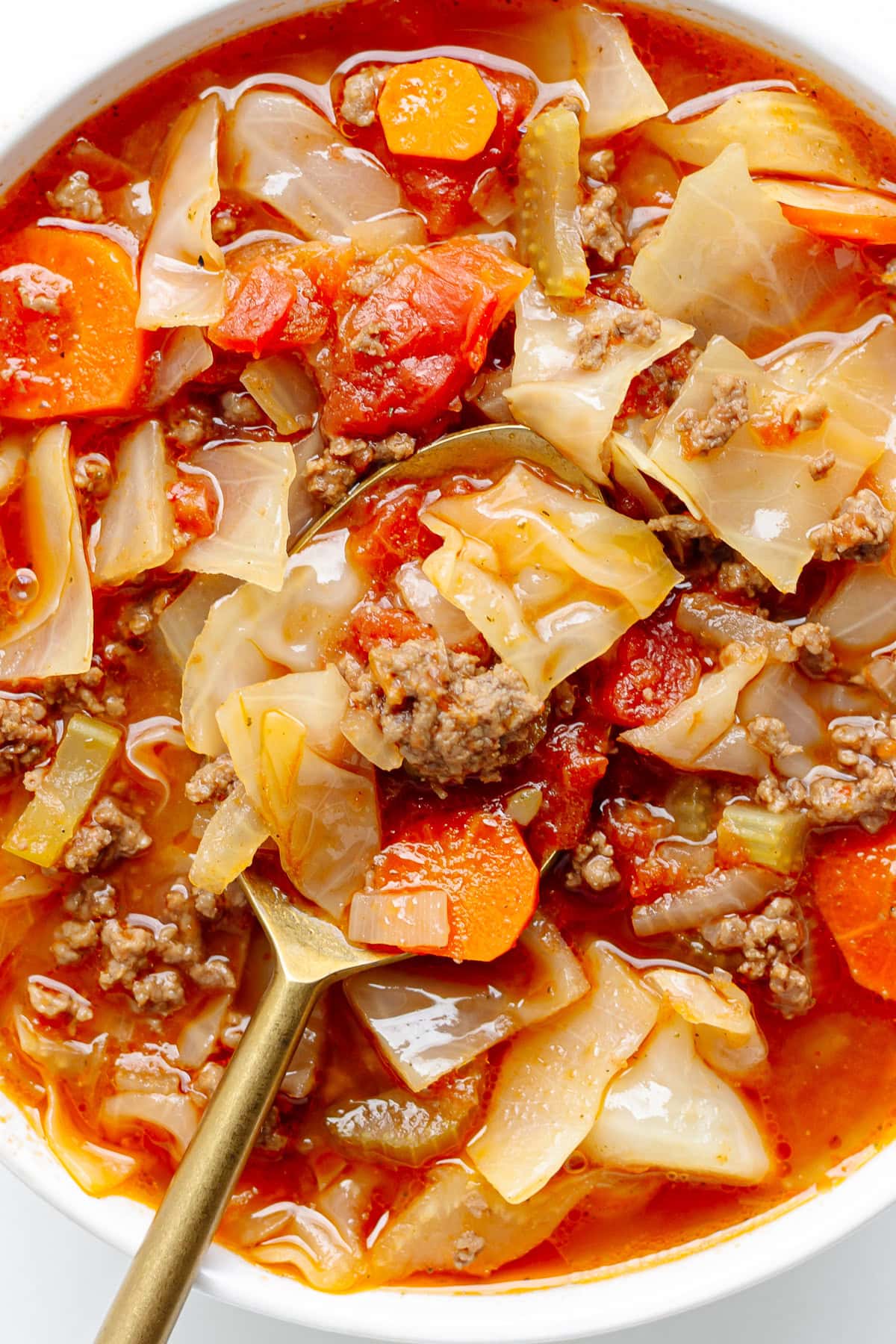 Cabbage soup with ground beef in a white bowl with spoon.