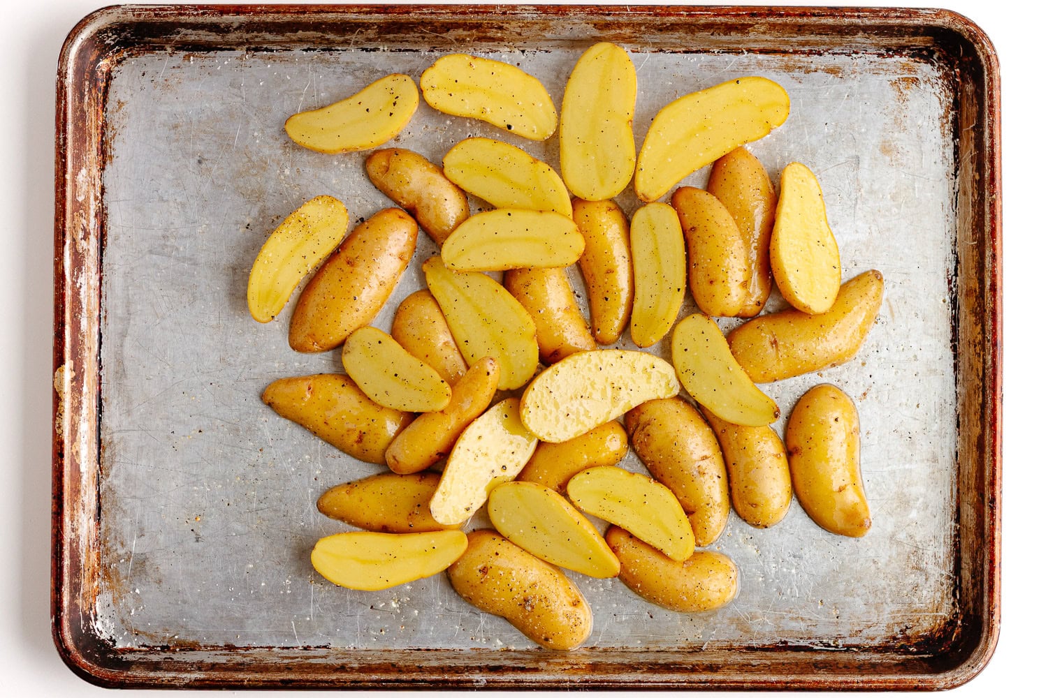 Halved fingerling potatoes on a baking sheet tossed with avocado oil, salt and pepper for roasting.