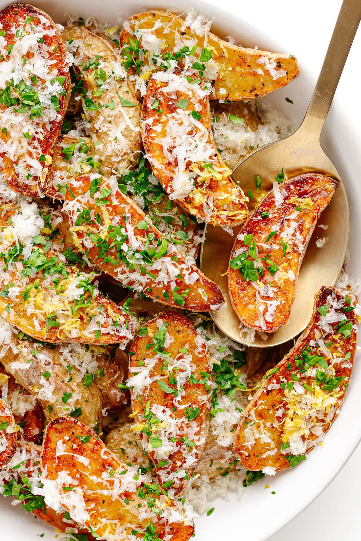 Roasted fingerling potatoes with truffle and parmesan in a serving bowl with serving spoon.