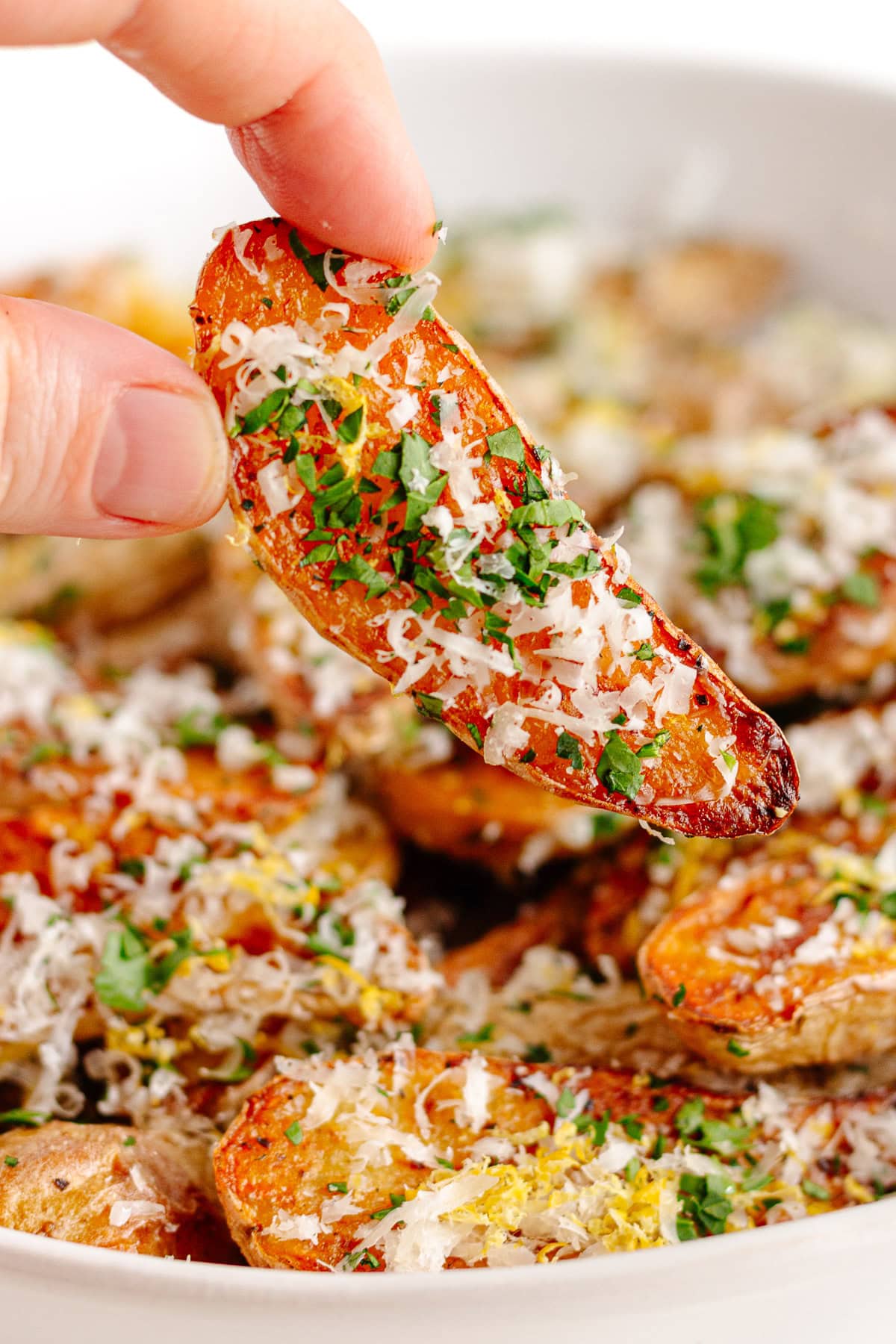 Hand picking up a truffle parmesan fingerling potato from bowl.