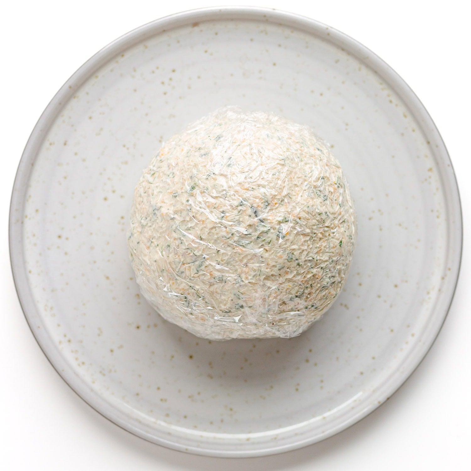 Spring cheese ball mixture formed into a ball and wrapped in plastic wrap.
