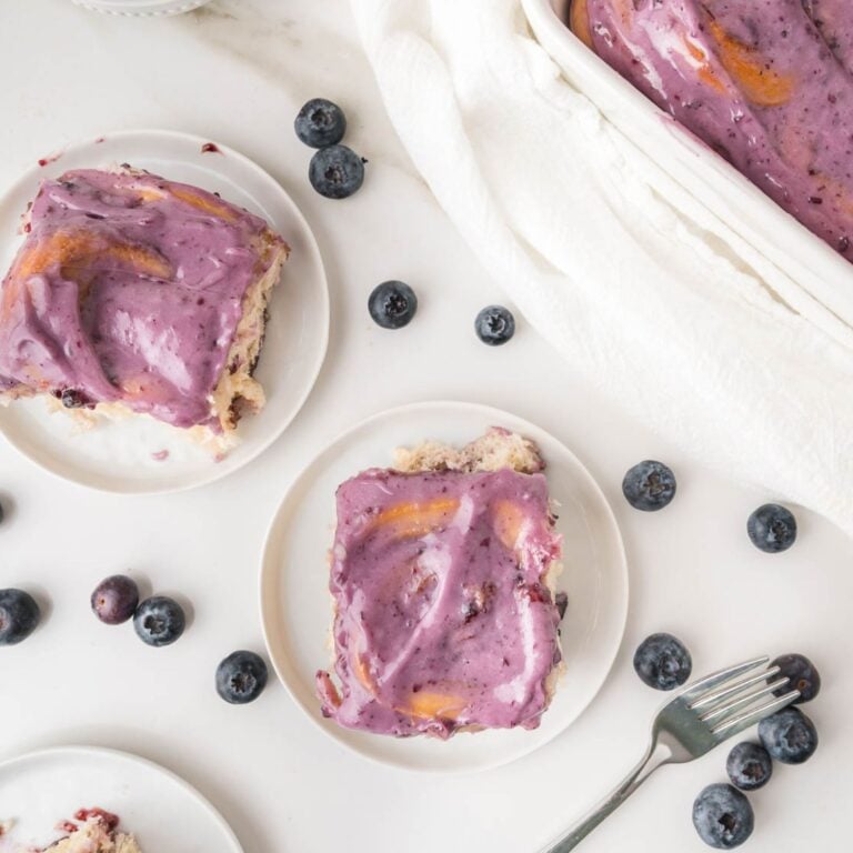 Plated blueberry cinnamon rolls on a white surface with scattered fresh blueberries.