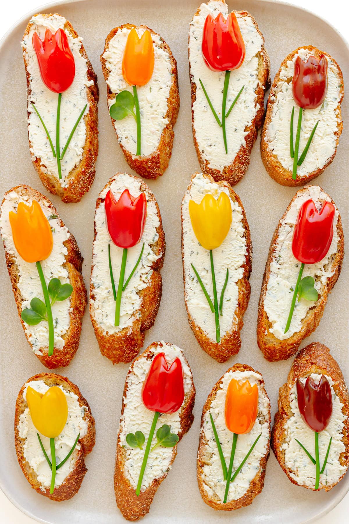 A spring themed crostini appetizer topped with tomato tulips on a serving platter.