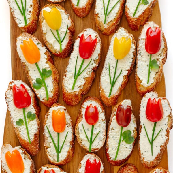 Spring crostini appetizer with tomato tulips on a wood serving board.