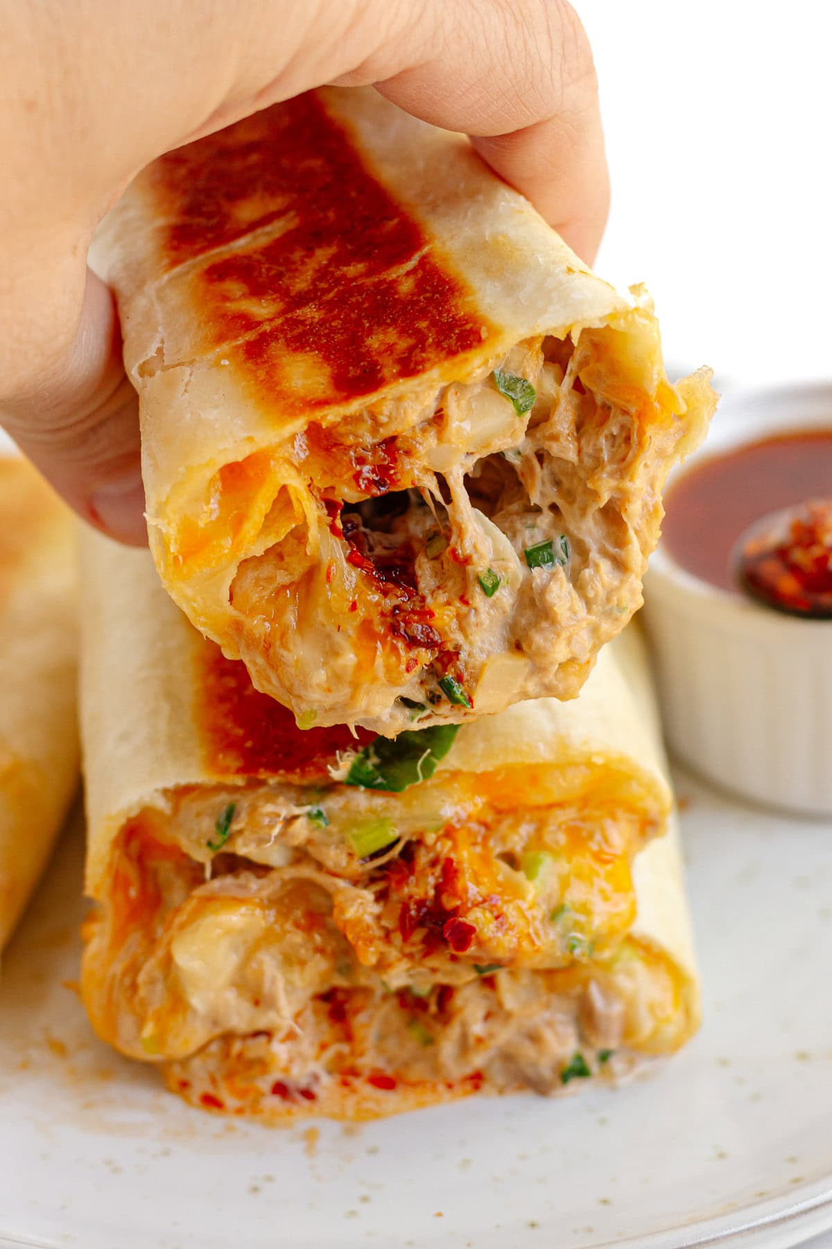 Hand picking up a chili crisp tuna melt wrap from a plate.