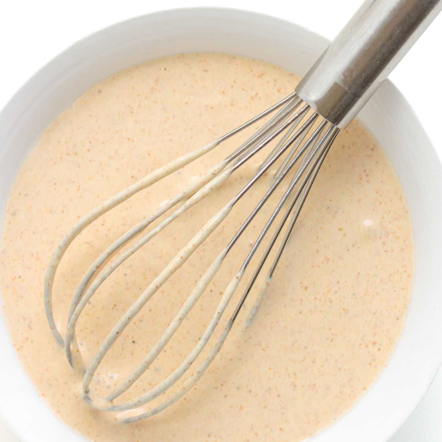Creamy dressing for dill pickle potato salad being whisked in a white bowl.