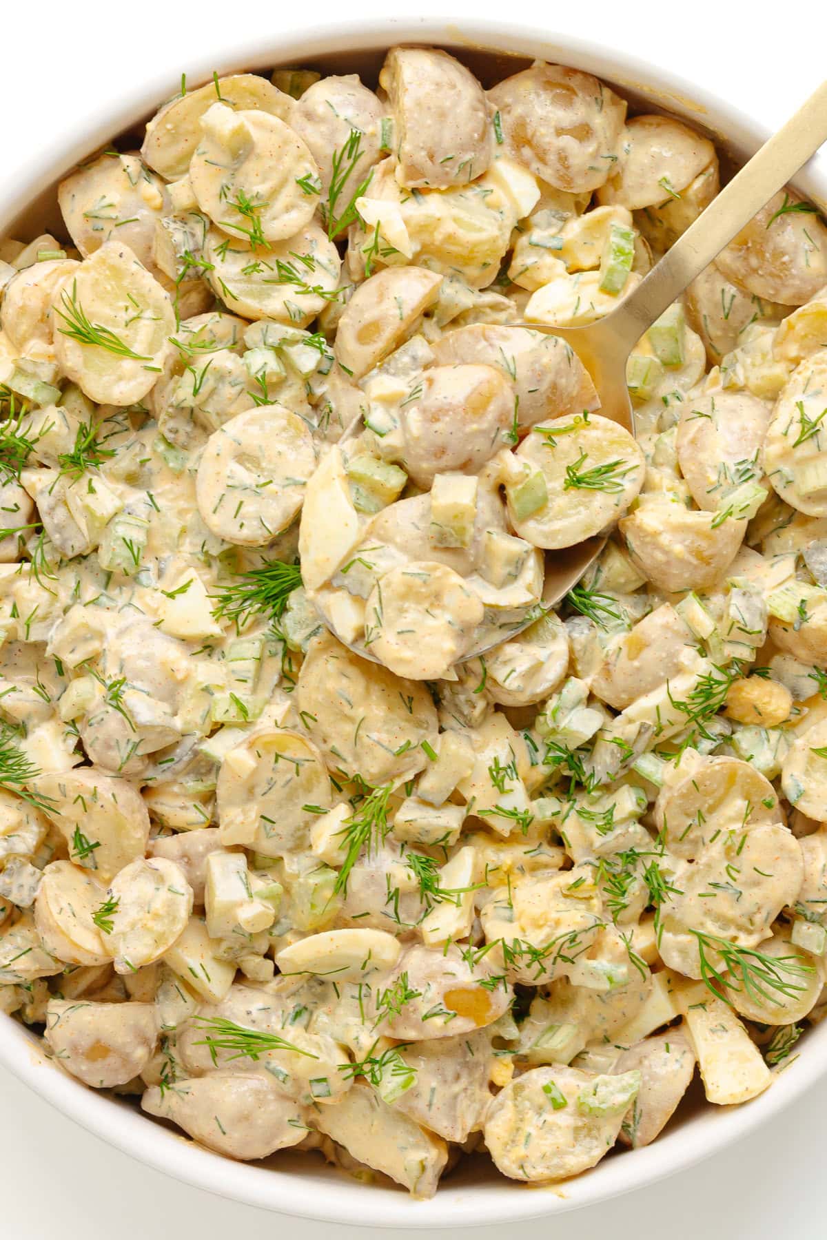 Dill pickle potato salad in a white serving bowl with serving spoon.