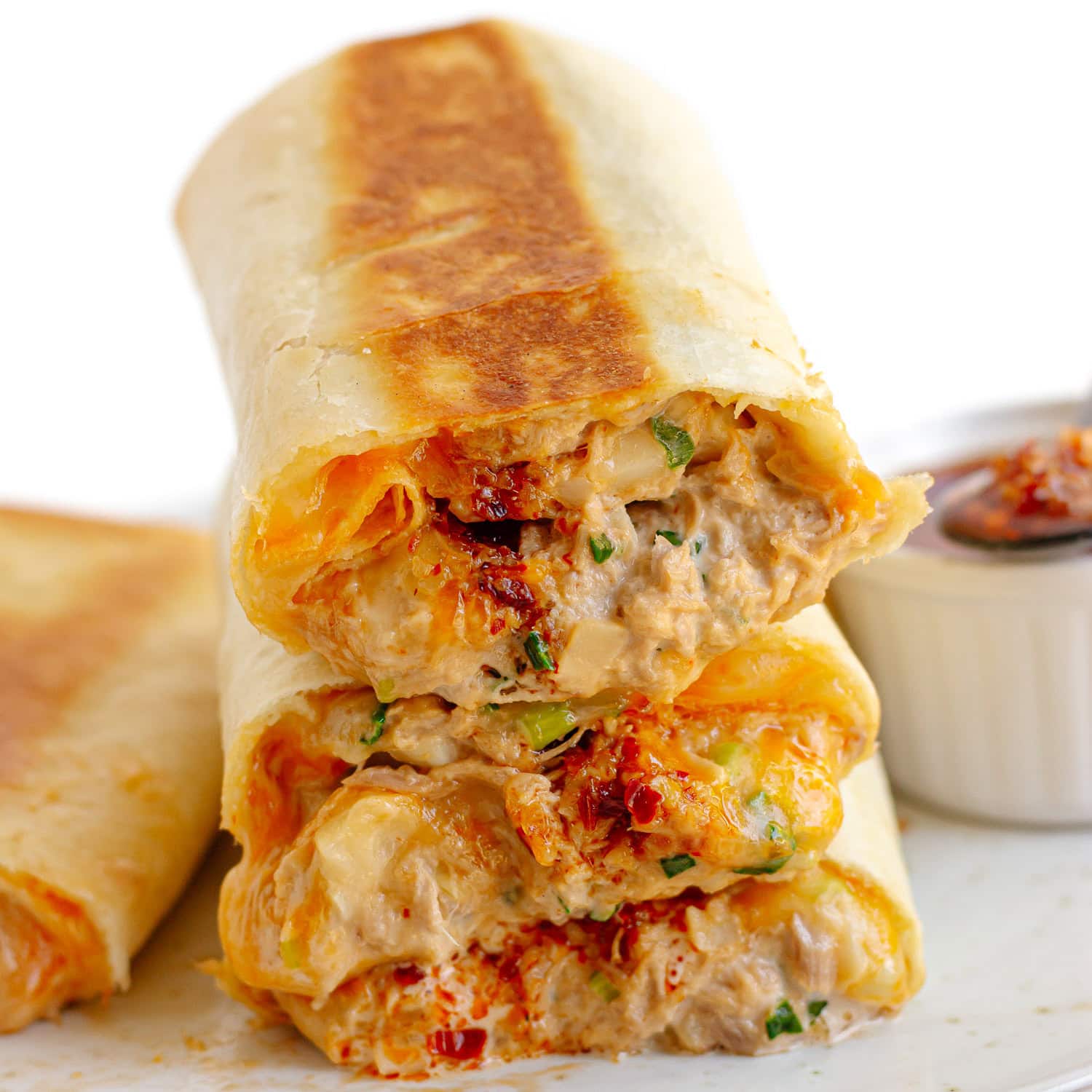Spicy tuna melt wraps sliced in half and piled up next to small bowl of chili crisp.