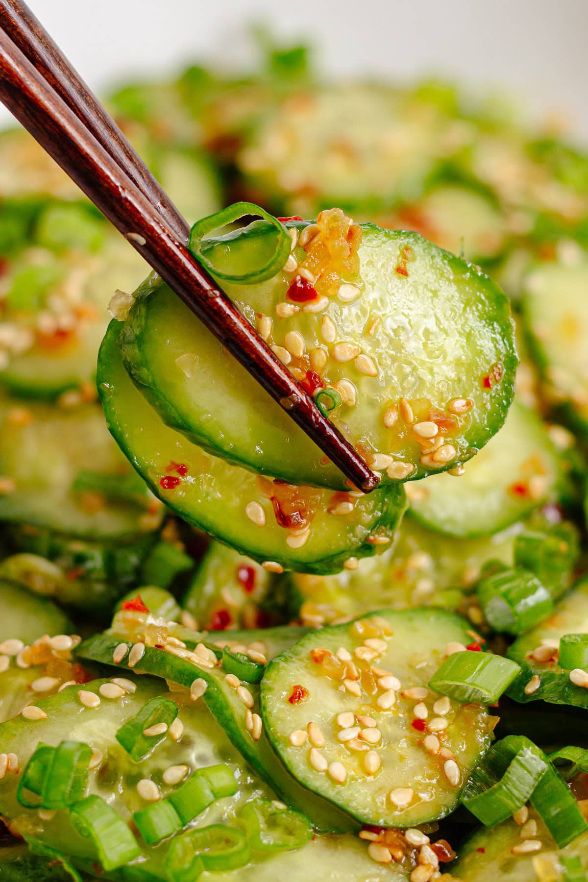 Chopsticks picking up some Asian cucumber salad with chili crisp.