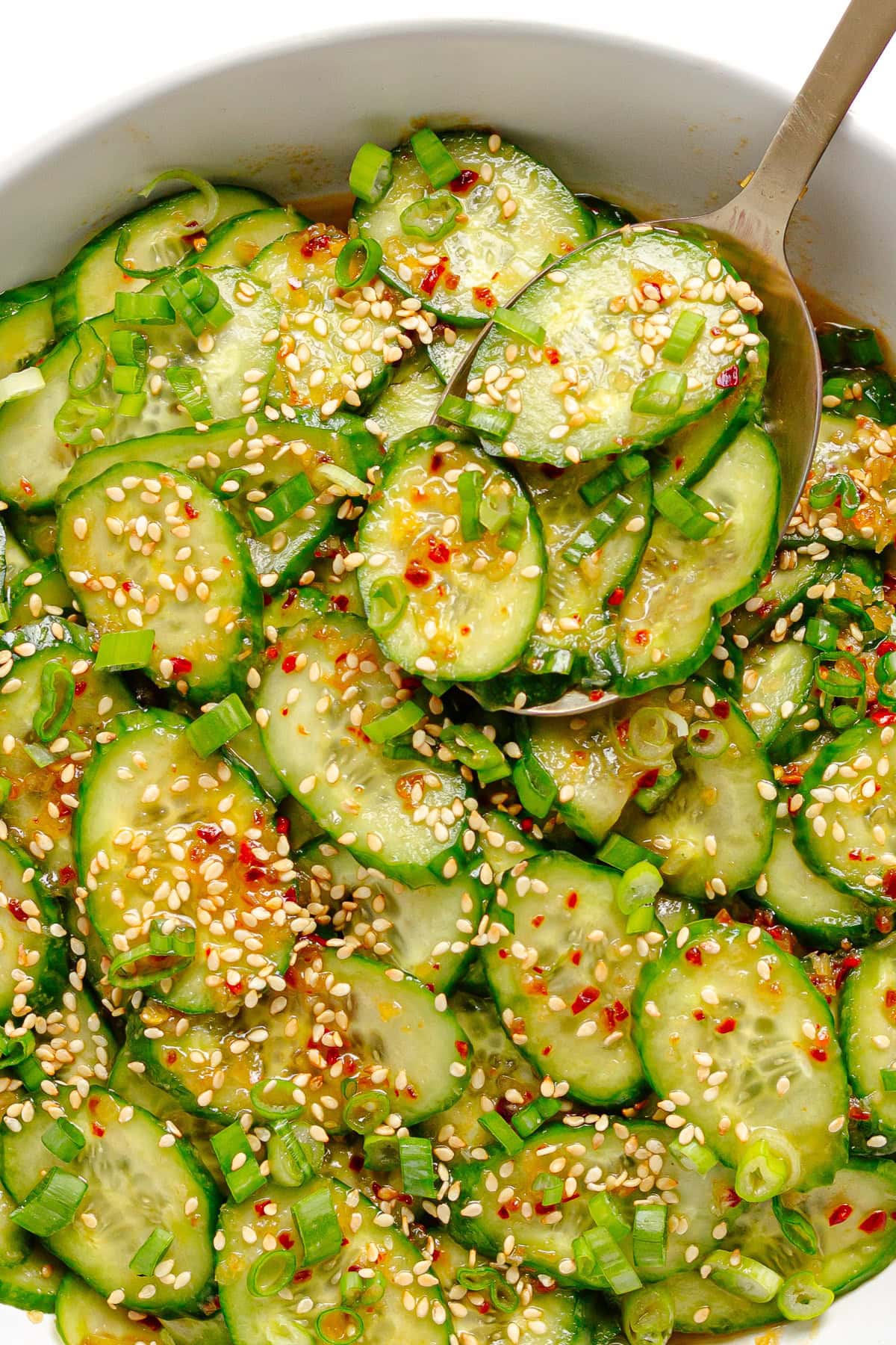 Serving spoon lifting some chili crisp cucumber salad from bowl.