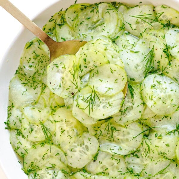 Serving spoon picking up some cucumber dill salad from bowl.