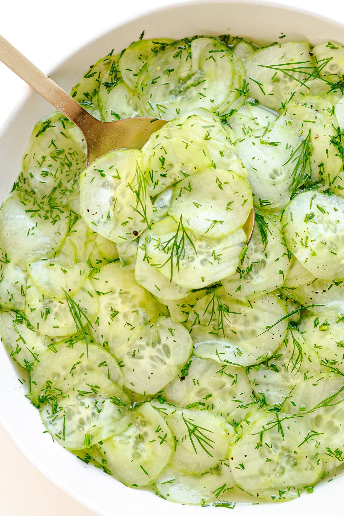 Cucumber dill salad in white serving bowl with gold colored serving spoon.