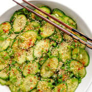 Spicy chili crisp cucumber salad in a white bowl with chopsticks set across a corner.