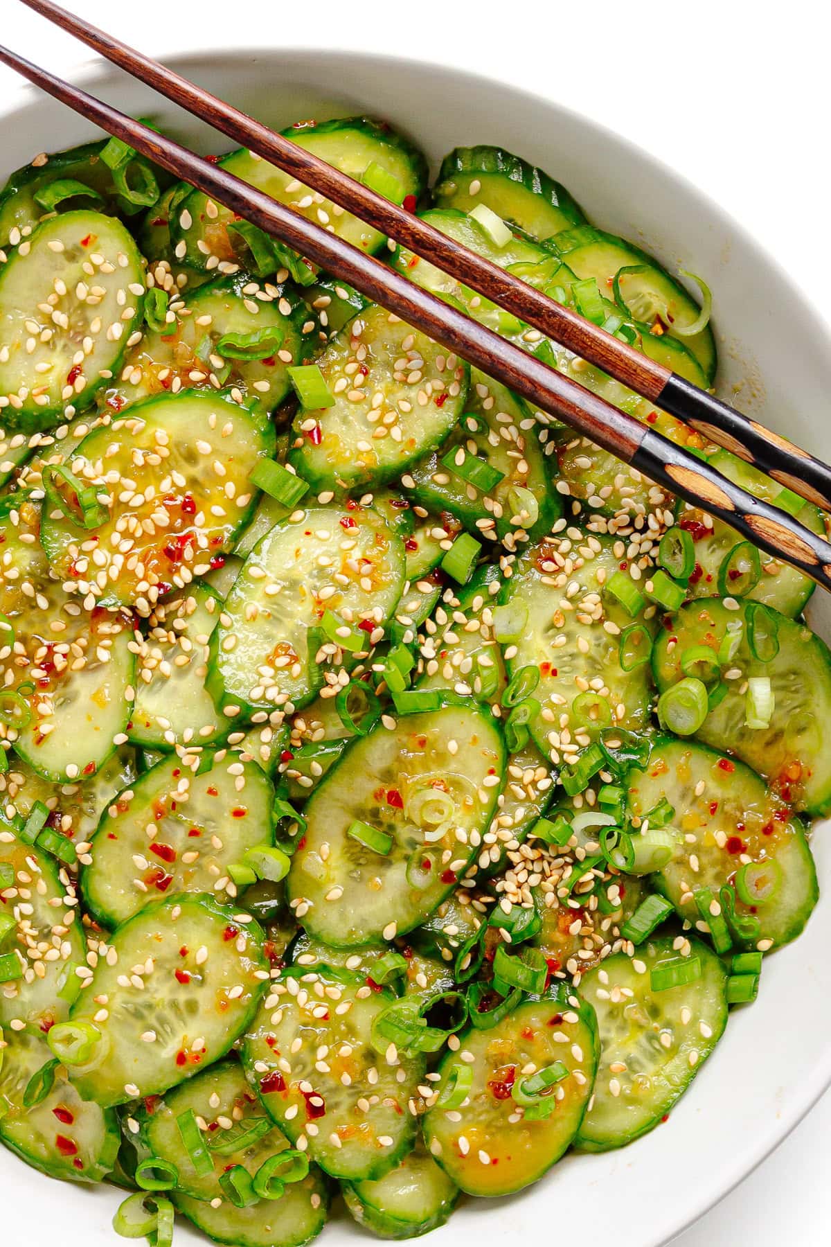 Spicy chili crisp cucumber salad in white bowl with chopsticks.