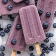 Blueberry yogurt popsicles piled on ice with fresh blueberries scattered around.
