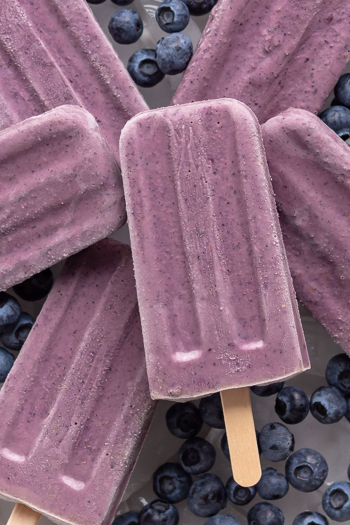 Pile of blueberry yogurt popsicles with fresh blueberries scattered around them.
