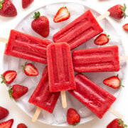 Strawberry popsicles arranged on a plate of ice with fresh strawberries.