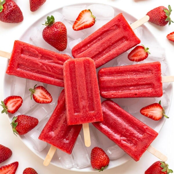 Strawberry popsicles arranged on a plate of ice with fresh strawberries.