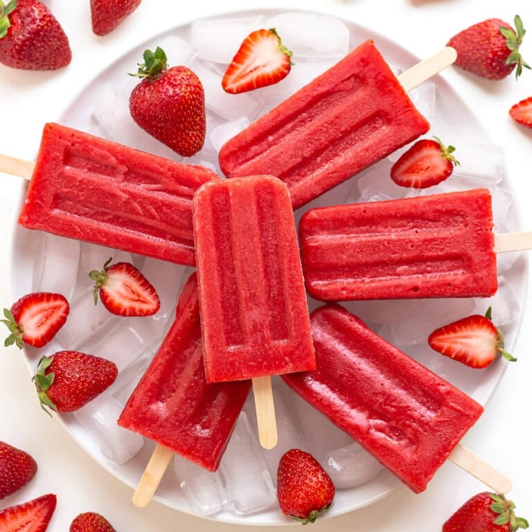 Strawberry popsicles arranged on a plate of ice with fresh strawberries.