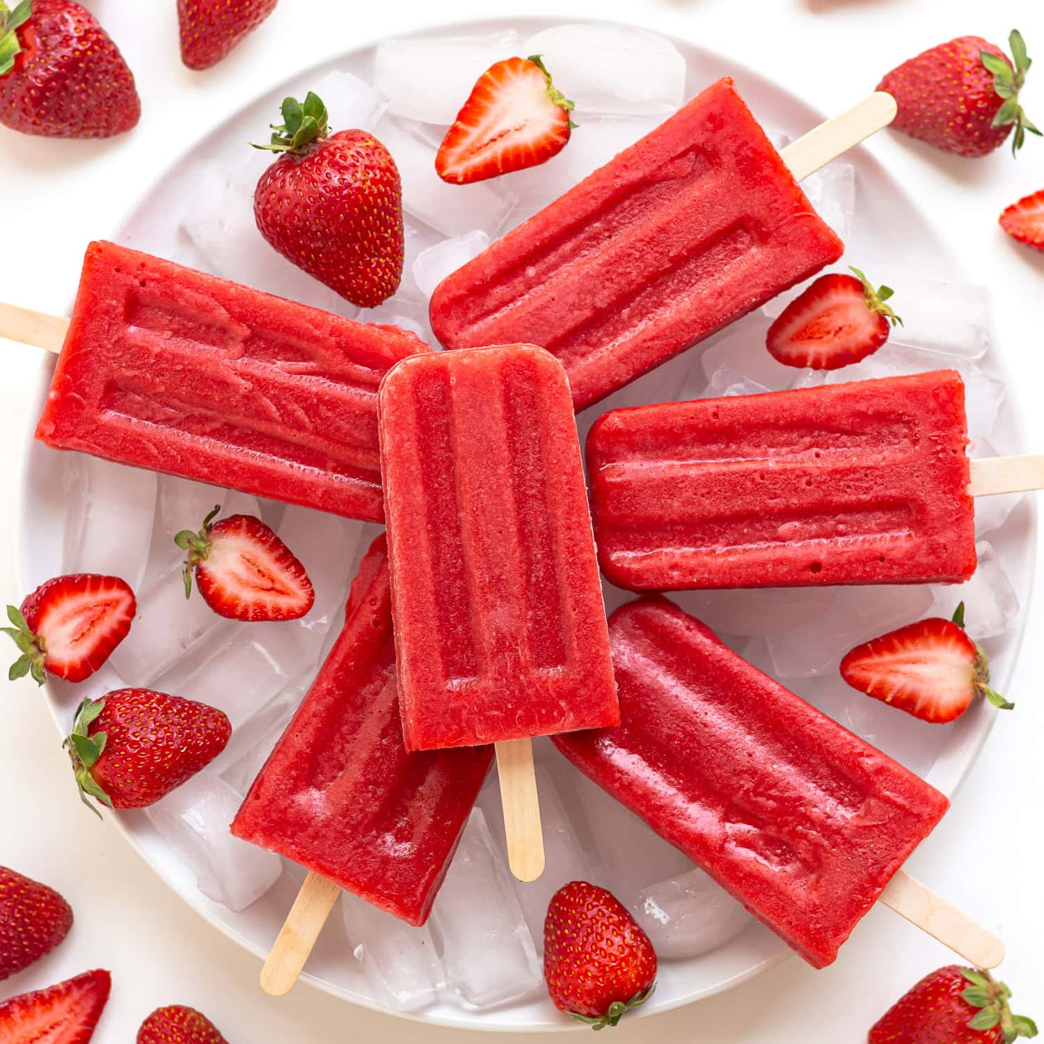 Strawberry popsicles arranged on a plate of ice with fresh strawberries.
